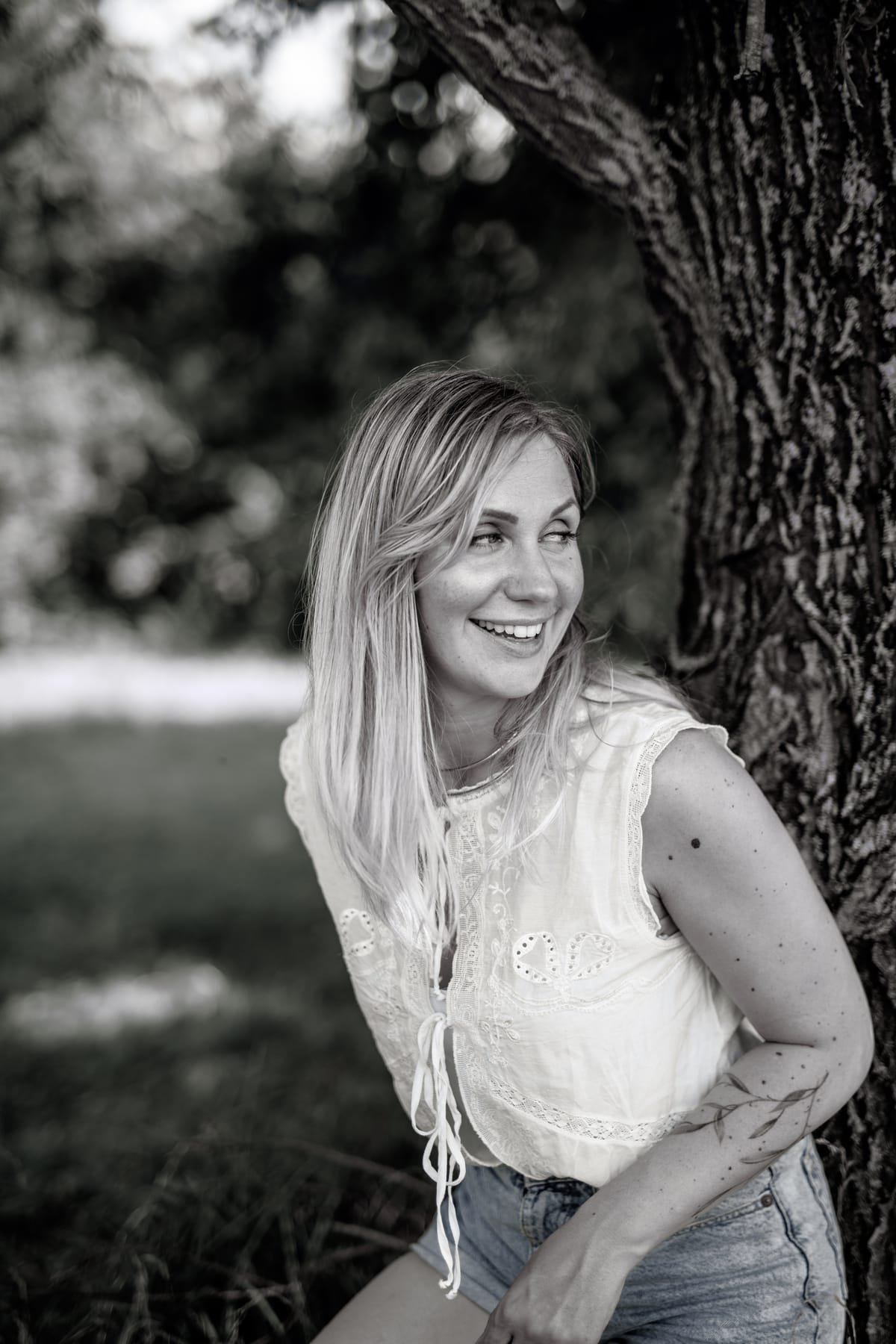 Portrait en noir et blanc, jeune femme souriante contre un arbre